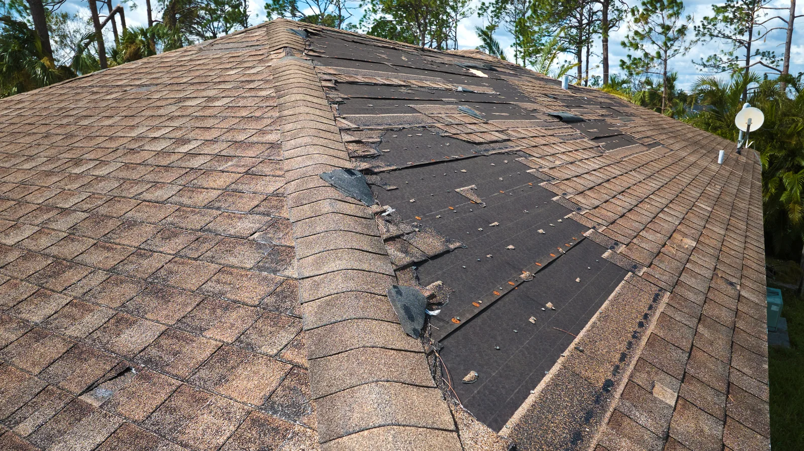 Large patches of shingles missing from a brown hip roof